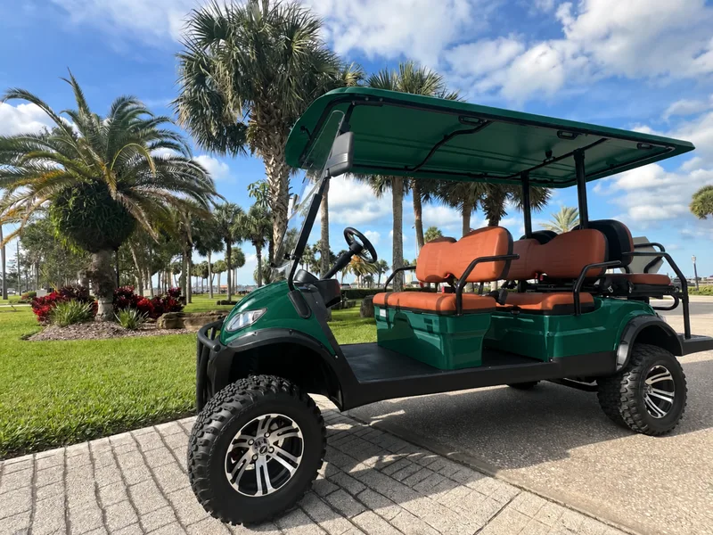 Forest green six-seat golf cart with orange seats parked on a paver path beneath palm trees