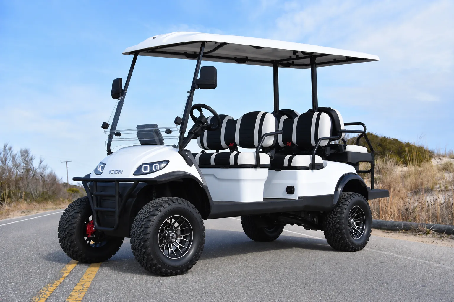 White six-seat golf cart with striped seats on a coastal road