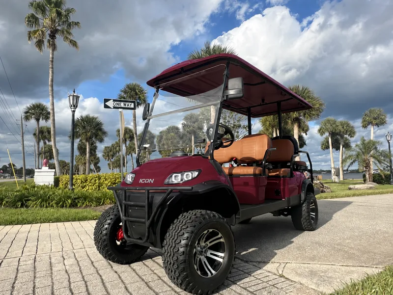 Sangria red six-seat ICON golf cart with tan seats on a palm-lined street